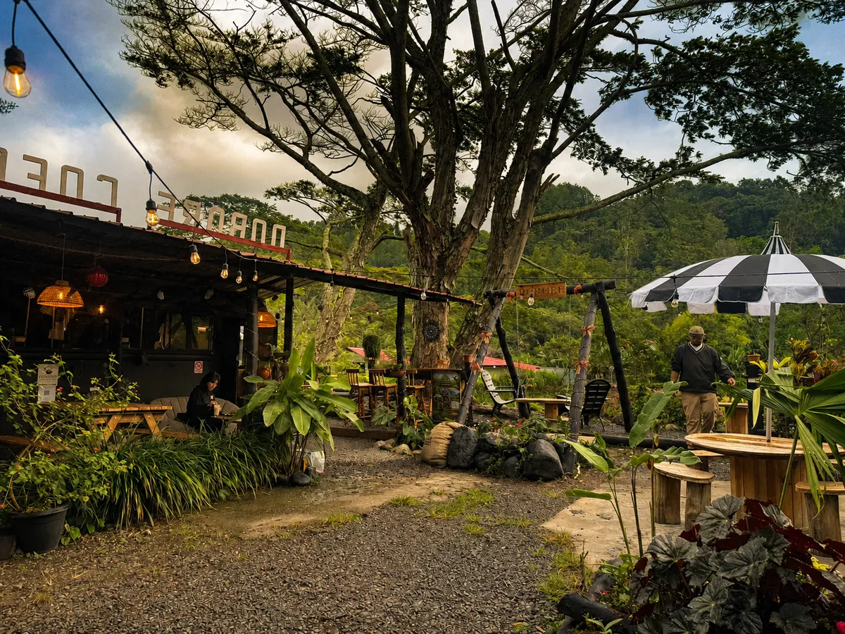 Mesas al aire libre bajo el árbol, con sombrilla a rayas y letrero de Dobore